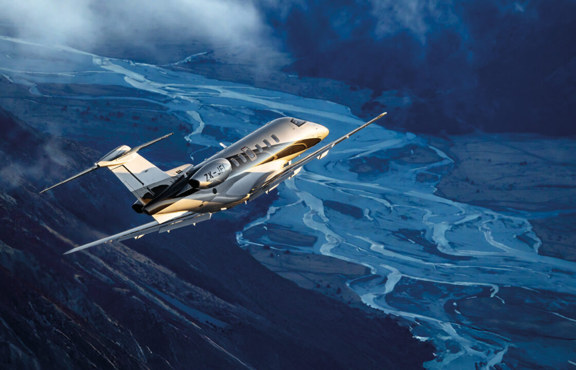Private jet flying over a mountain valley with winding rivers below during sunset