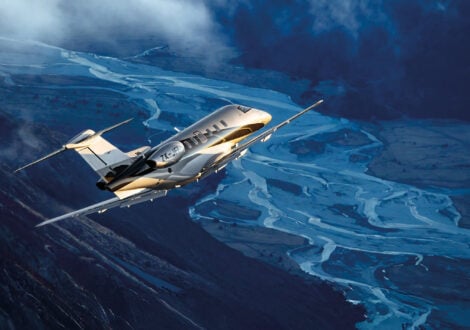 Private jet flying over a mountain valley with winding rivers below during sunset