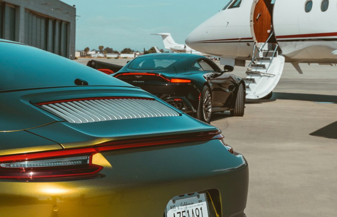Private jet charter with luxury sports cars parked beside the aircraft on the apron
