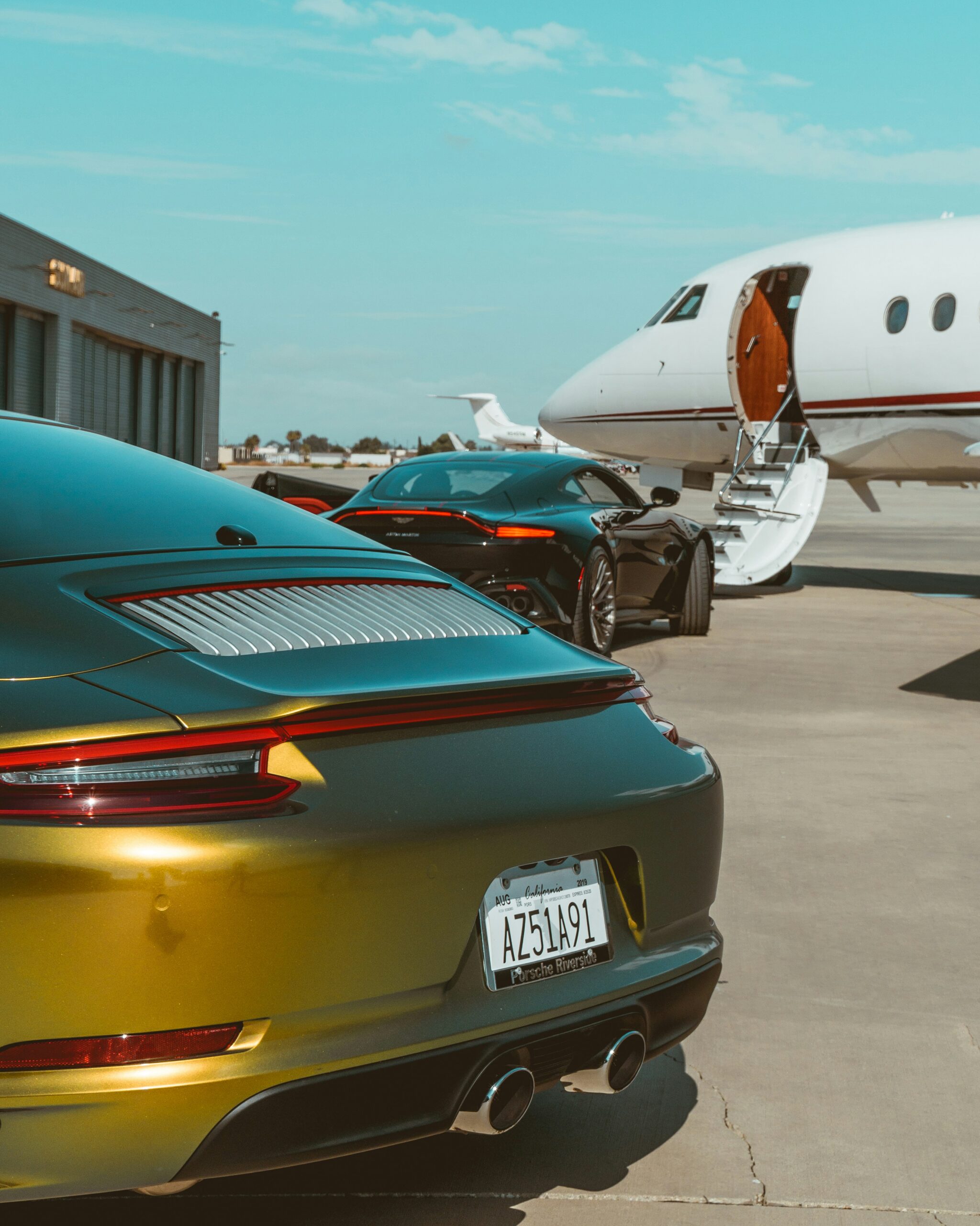 Private jet charter with luxury sports cars parked beside the aircraft on the apron