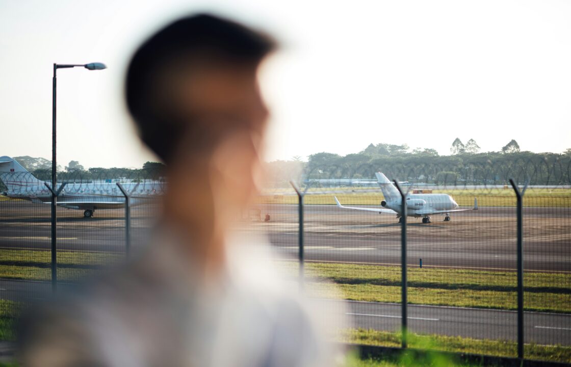Traveler looking at private jets parked on the airport apron behind a fence