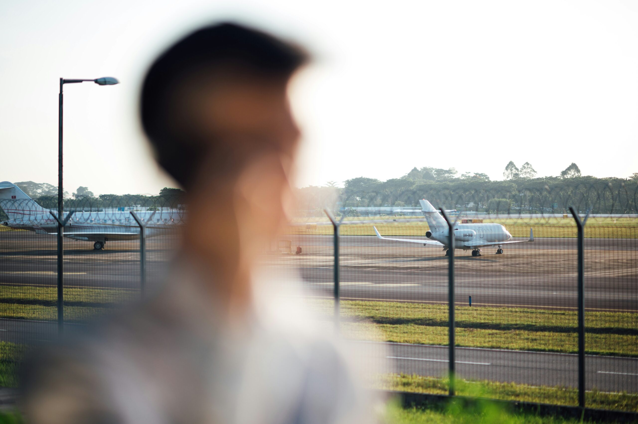 Traveler looking at private jets parked on the airport apron behind a fence